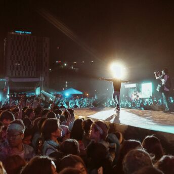 A large crowd at a night concert with bright lights and a performer on stage