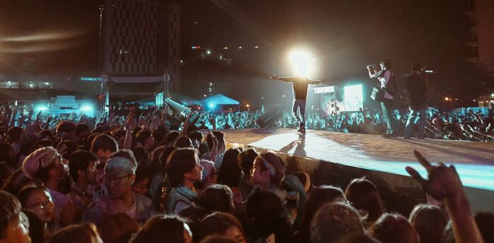 A large crowd at a night concert with bright lights and a performer on stage
