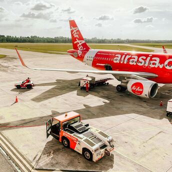 AirAsia aircraft parked on an airport tarmac with ground support vehicles nearby