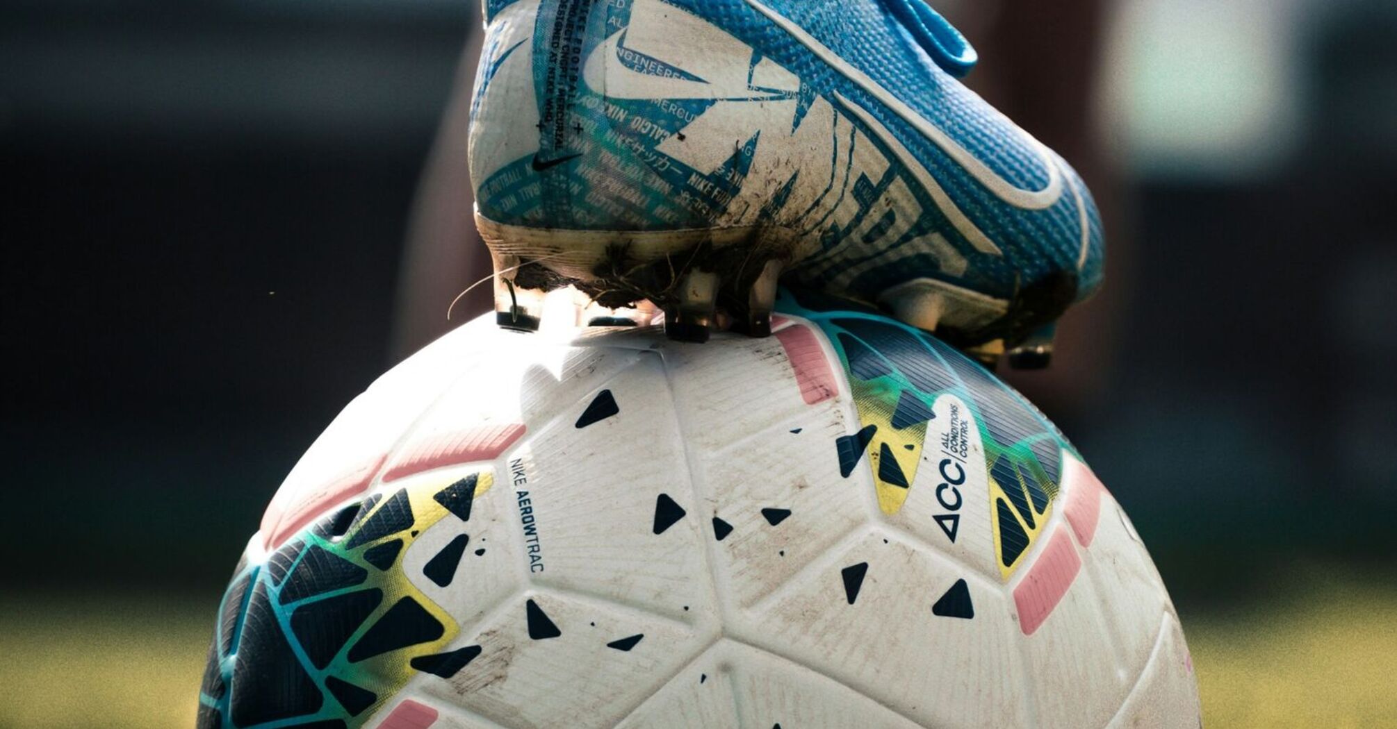 A close-up of a soccer cleat resting on a soccer ball on a grassy field, suggesting an active moment in sports