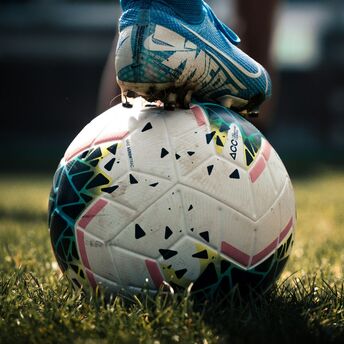 A close-up of a soccer cleat resting on a soccer ball on a grassy field, suggesting an active moment in sports