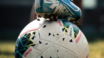 A close-up of a soccer cleat resting on a soccer ball on a grassy field, suggesting an active moment in sports
