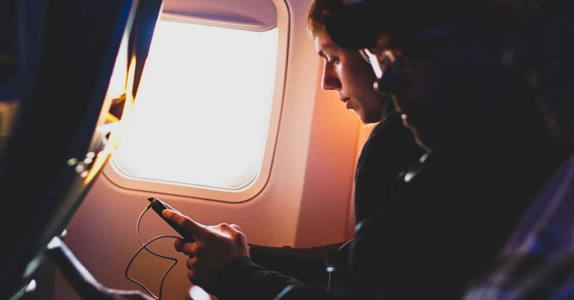 A person sitting by an airplane window, looking at their phone during a flight