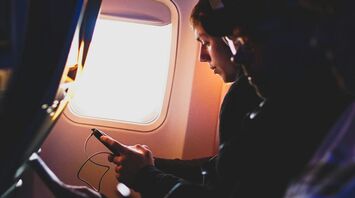 A person sitting by an airplane window, looking at their phone during a flight