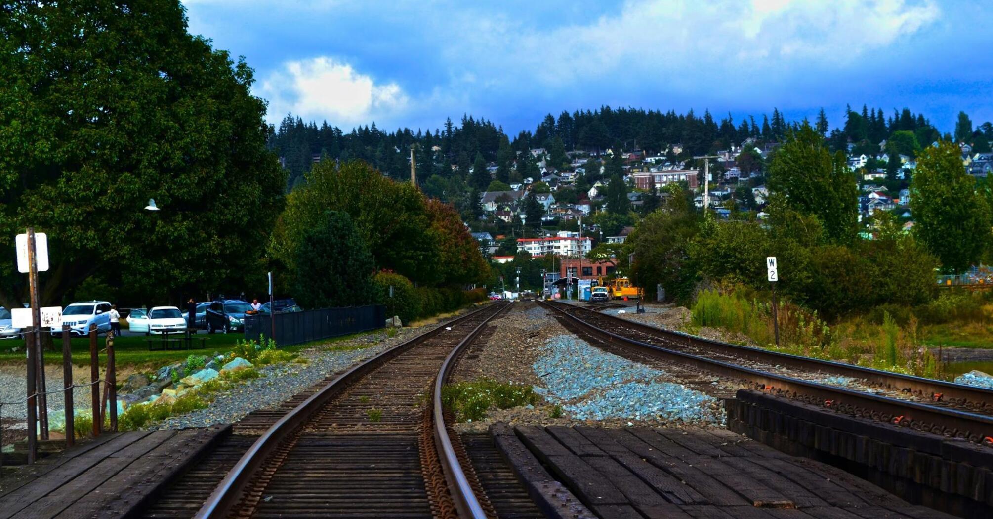 Railway tracks leading into a suburban town with trees and cars nearby