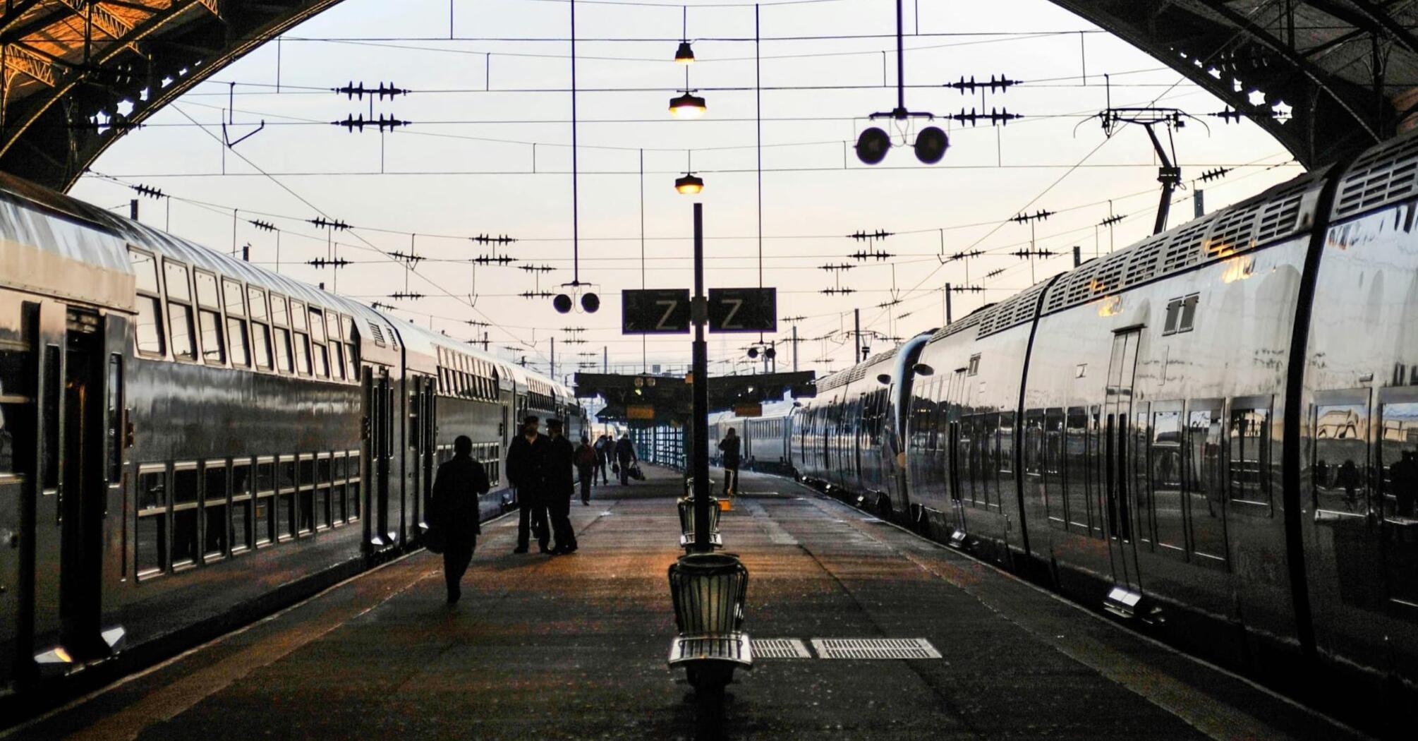 Busy train station platform with passengers boarding and disembarking trains in the evening light