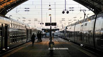 Busy train station platform with passengers boarding and disembarking trains in the evening light