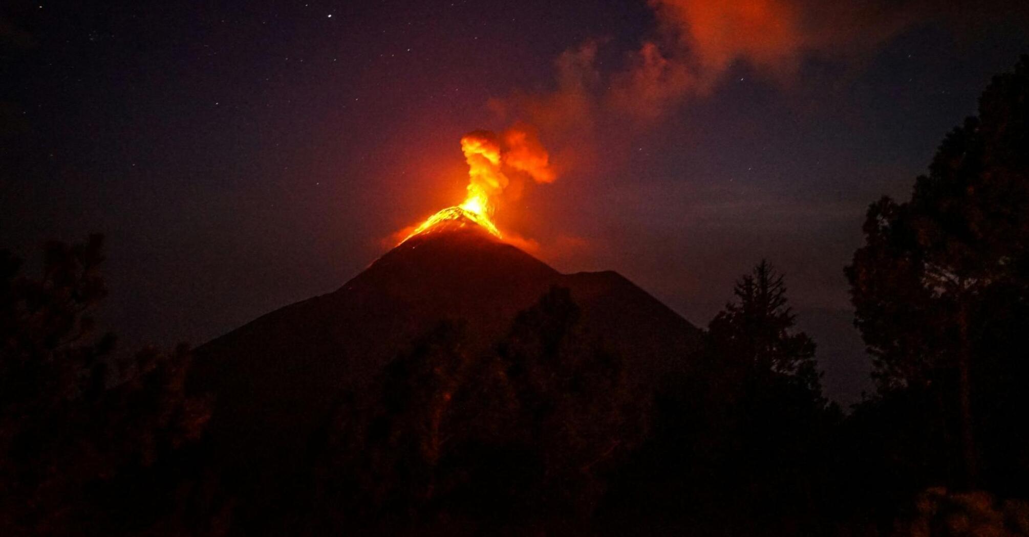 Erupting volcano spewing lava and smoke against a night sky