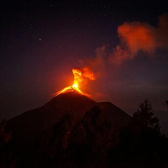 Erupting volcano spewing lava and smoke against a night sky