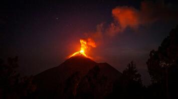 Erupting volcano spewing lava and smoke against a night sky
