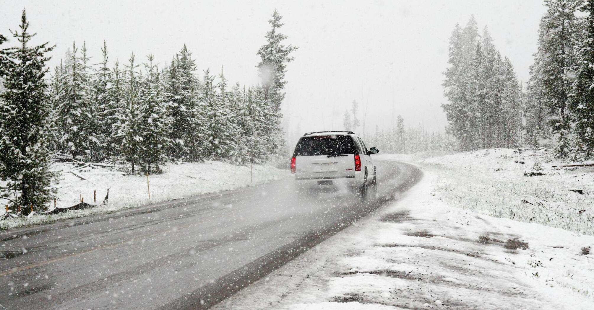 Car driving on a snowy road surrounded by trees