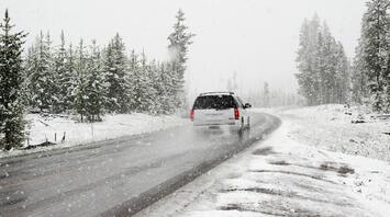 Car driving on a snowy road surrounded by trees