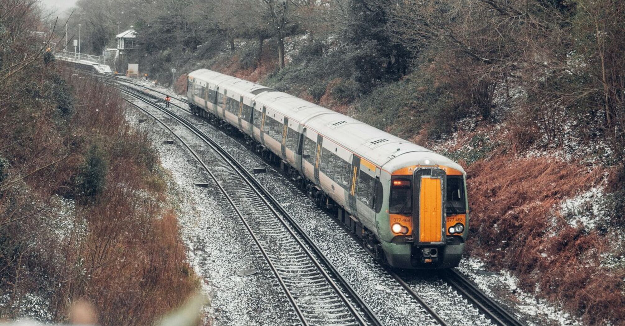 A train traveling through a snowy, rural landscape on a curved railway line, surrounded by bare winter trees