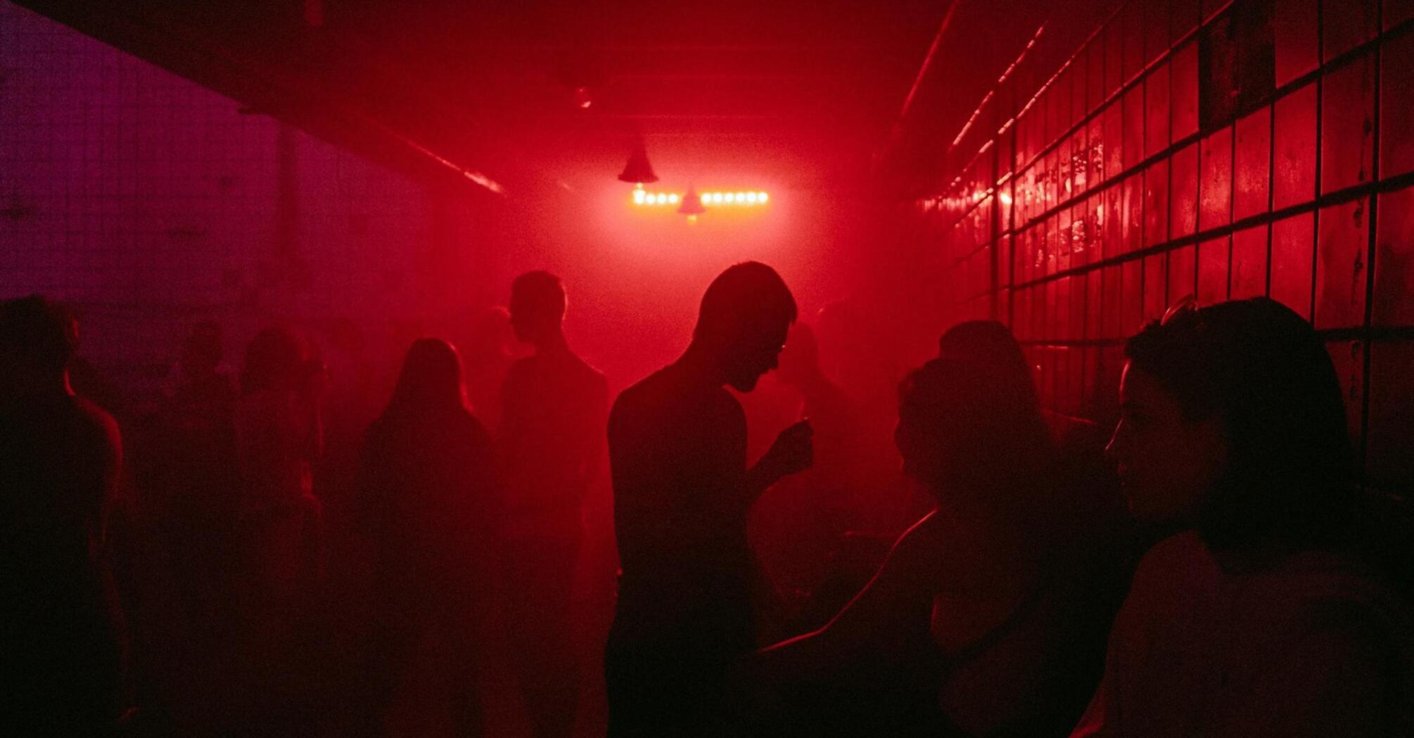 A dimly lit nightclub with people in red lighting