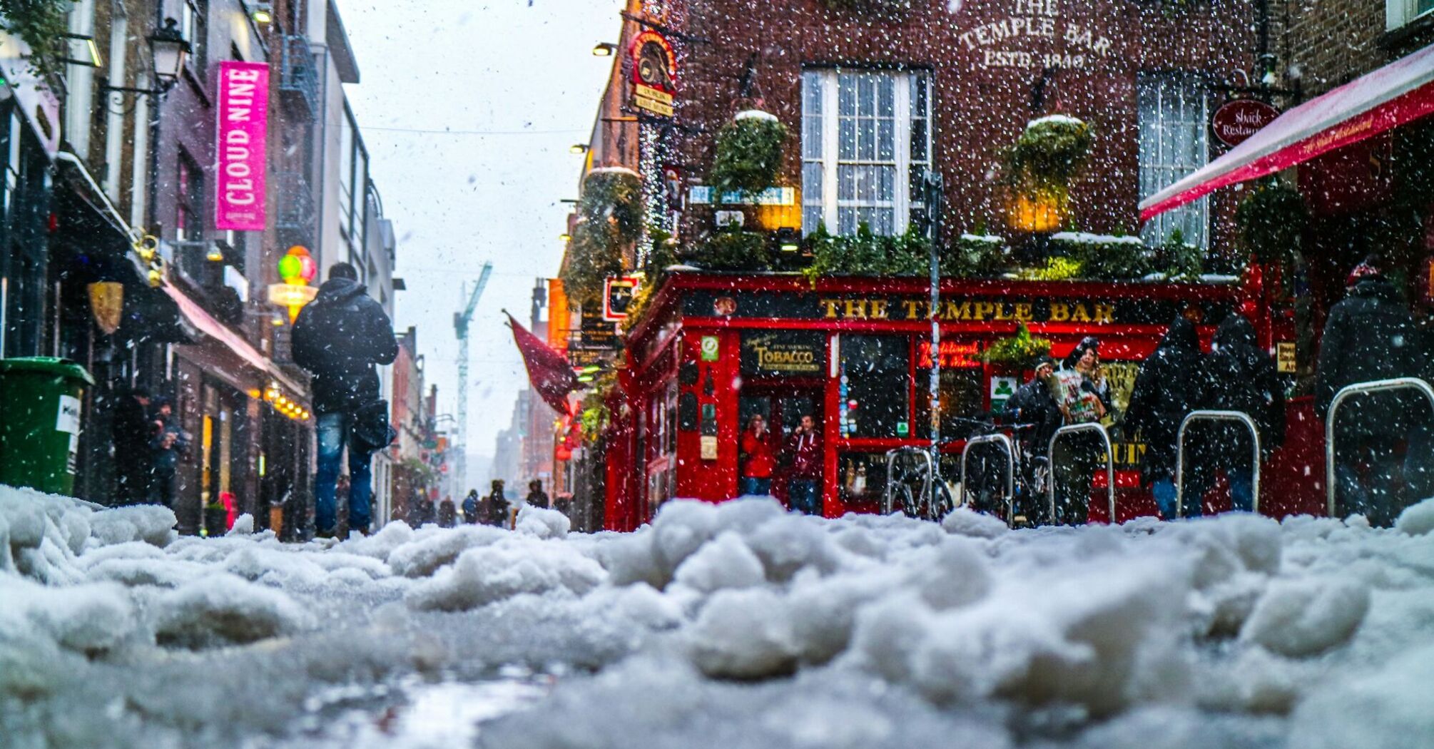 Snow-covered street with people walking in a bustling urban area outside a pub