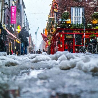 Snow-covered street with people walking in a bustling urban area outside a pub