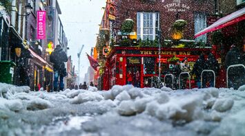 Snow-covered street with people walking in a bustling urban area outside a pub
