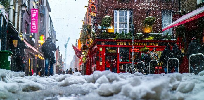 Snow-covered street with people walking in a bustling urban area outside a pub