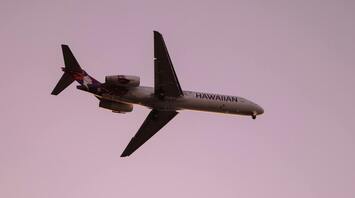 Hawaiian Airlines plane flying against a sunset sky