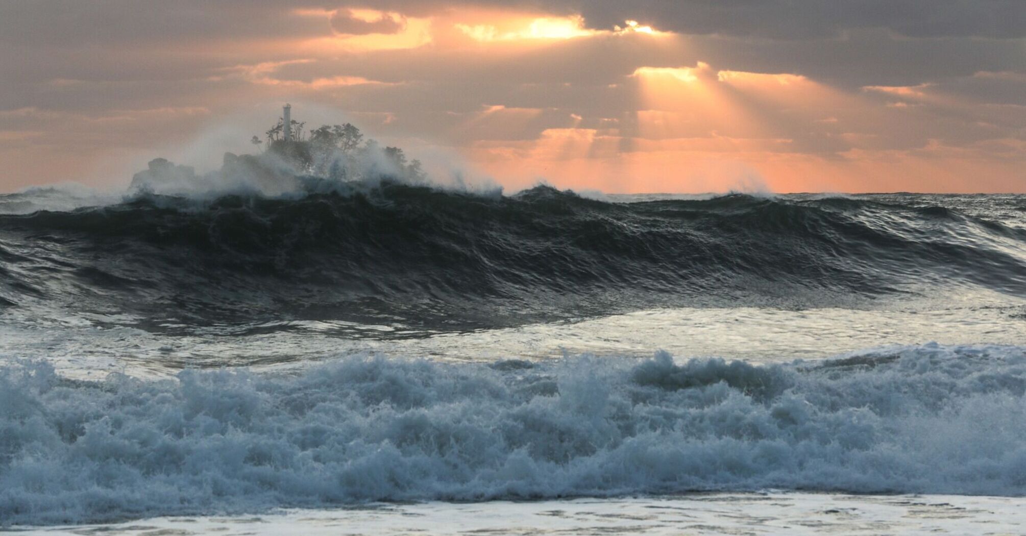 Powerful waves crash under a cloudy sunset