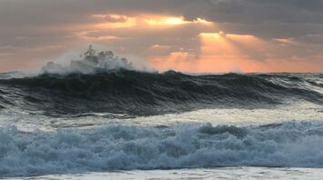 Powerful waves crash under a cloudy sunset