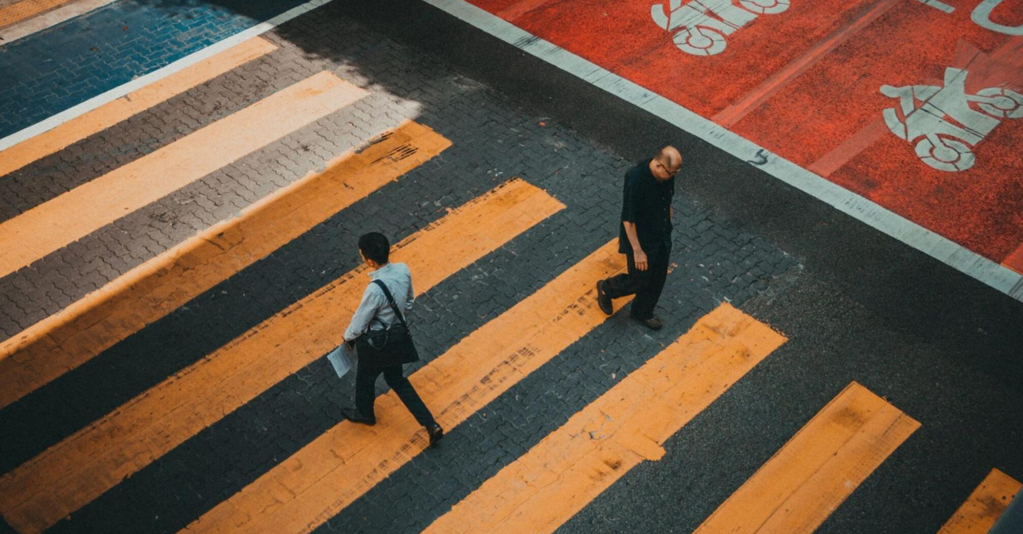 Two people crossing a striped crosswalk viewed from above