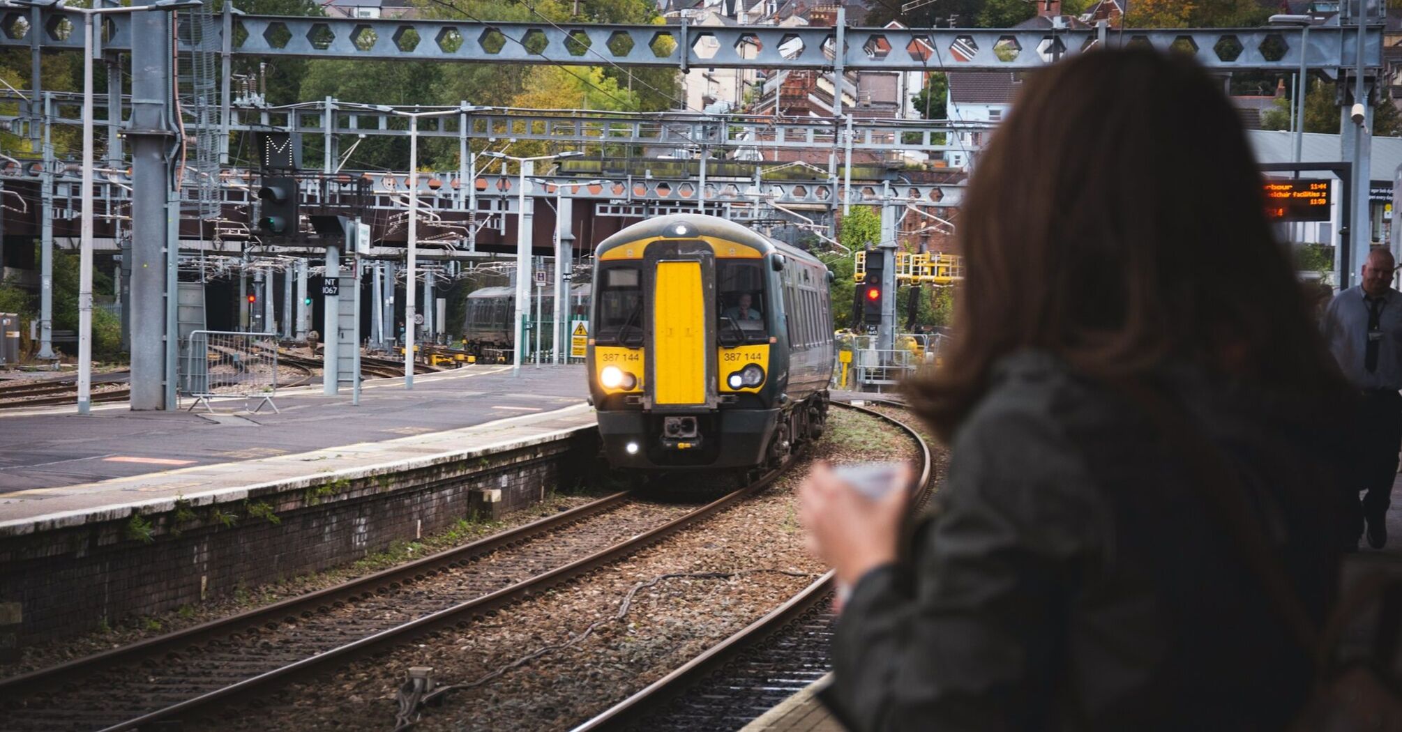 A train arrives at a platform with a waiting passenger observing its approach