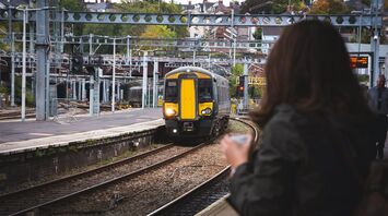 A train arrives at a platform with a waiting passenger observing its approach