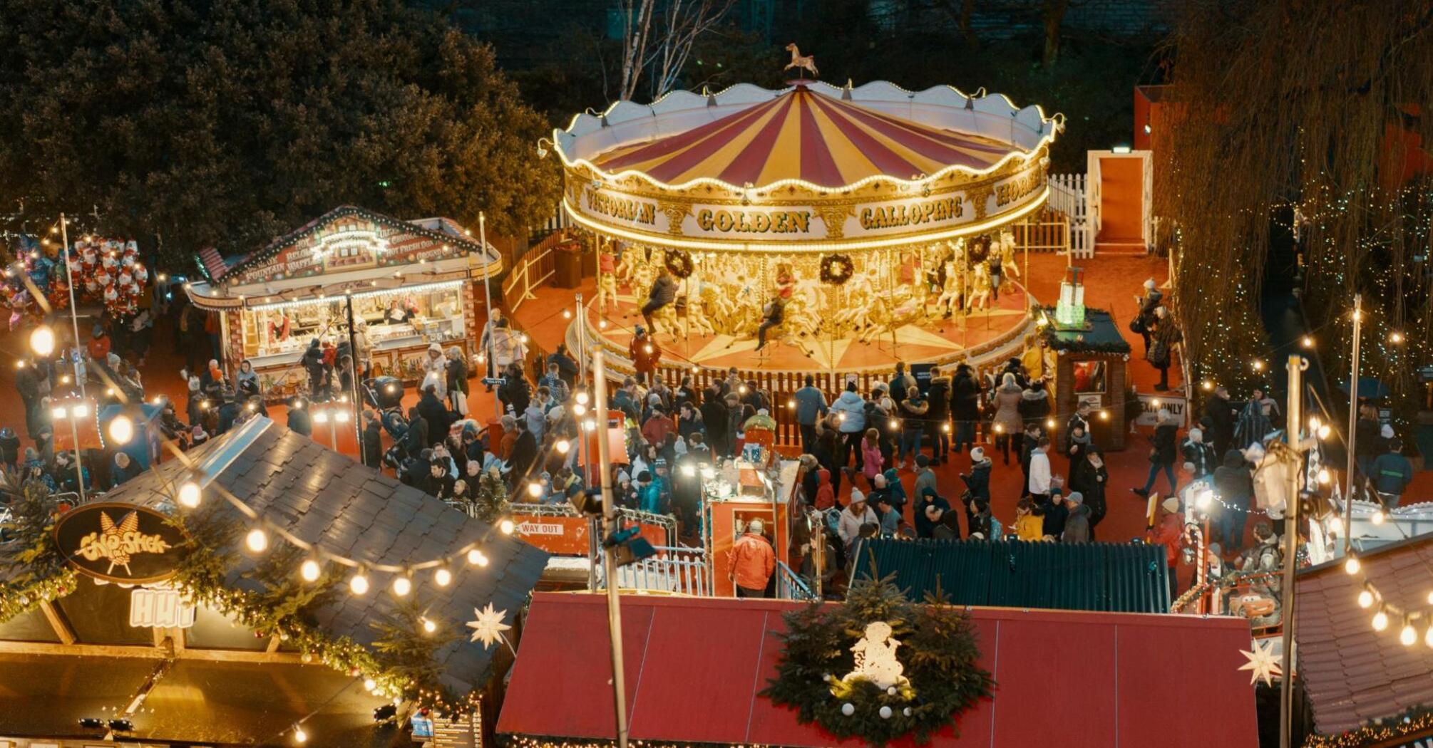 A vibrant Christmas market with a carousel and festive stalls, illuminated with warm lights, bustling with visitors in a holiday atmosphere