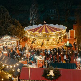 A vibrant Christmas market with a carousel and festive stalls, illuminated with warm lights, bustling with visitors in a holiday atmosphere
