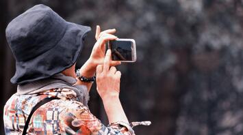 A person in colorful attire taking a photo with a smartphone outdoors