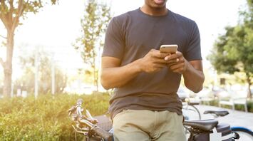 A person using a smartphone outdoors with bicycles nearby