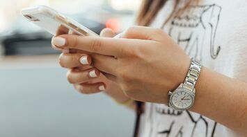Person holding a smartphone with a silver watch on wrist