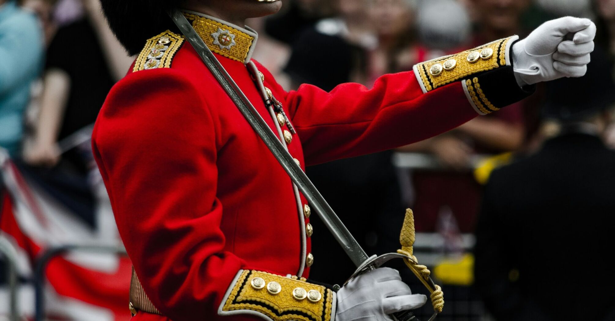 A soldier in a traditional red uniform holds a ceremonial sword during a British royal event