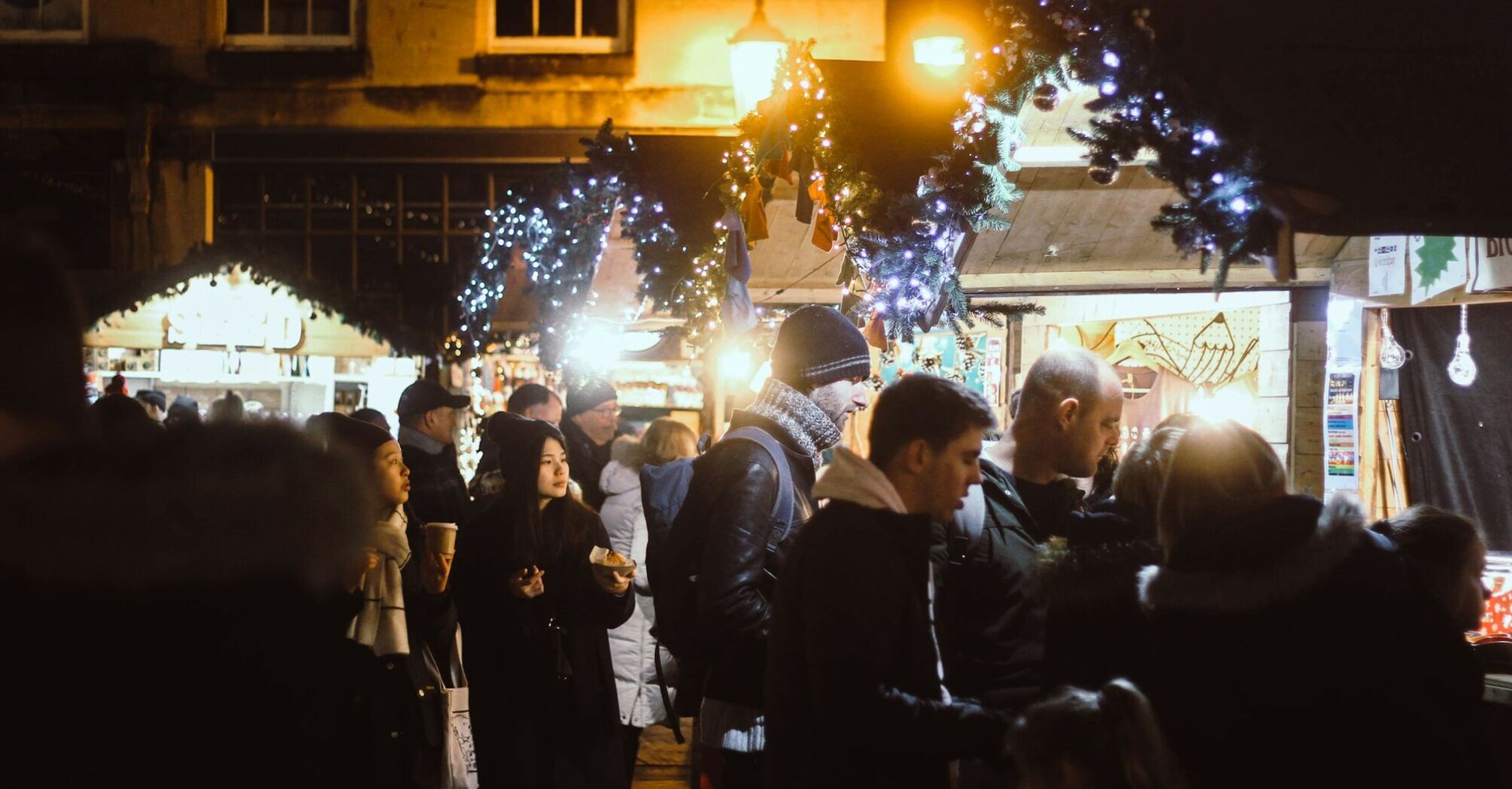 Crowds enjoying festive stalls and holiday lights at a Christmas market in the evening