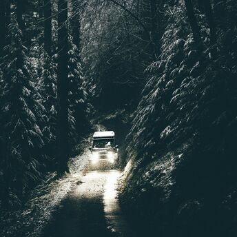 A car drives through a narrow, snowy forest road with dim lighting in Wales