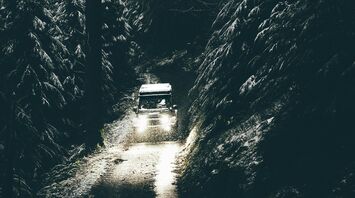 A car drives through a narrow, snowy forest road with dim lighting in Wales