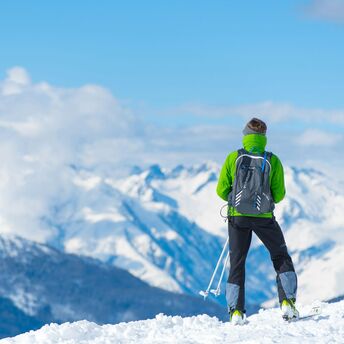 A skier in a green jacket overlooking snowy mountain peaks under a clear blue sky