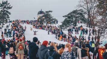 Crowds gather on a snowy hill during a winter festival in Helsinki, surrounded by trees and an observatory in the background