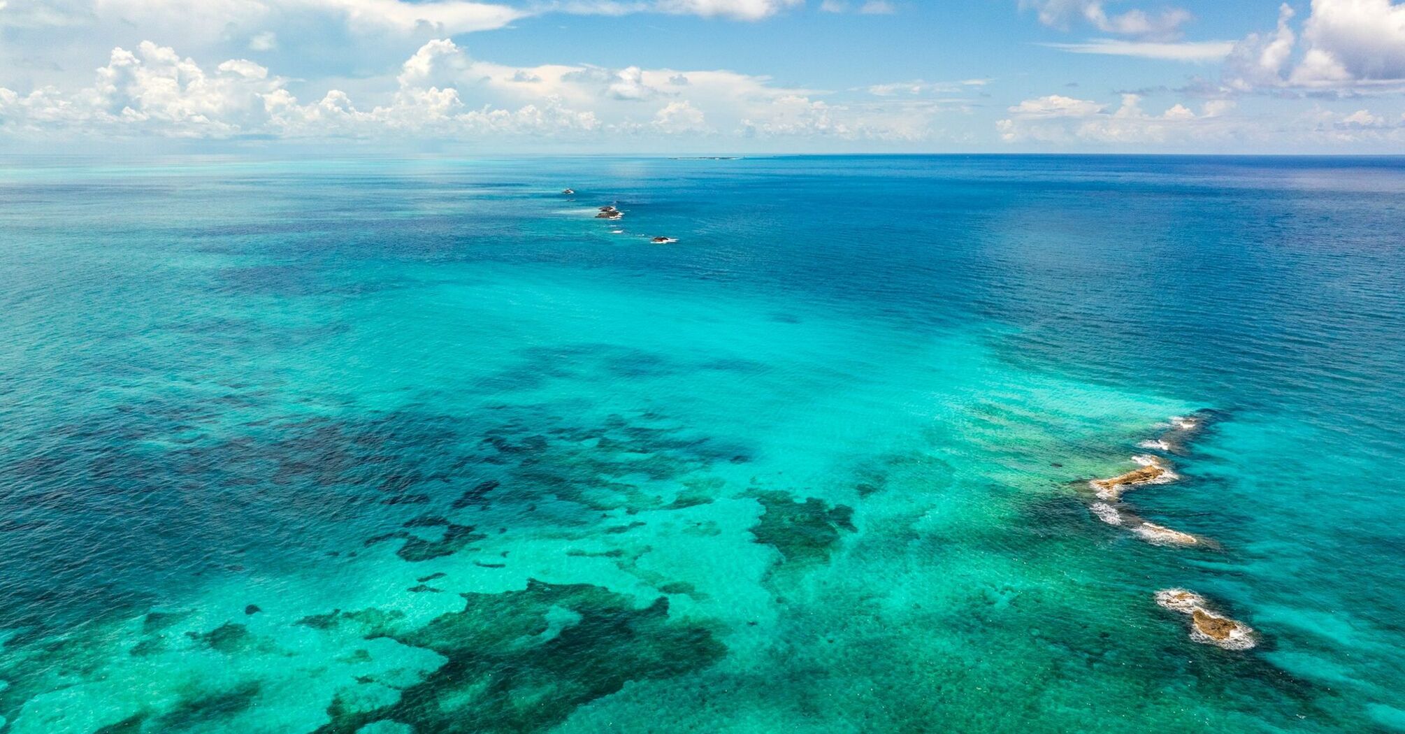 Aerial view of vibrant turquoise ocean waters with patches of coral reefs under a partly cloudy sky