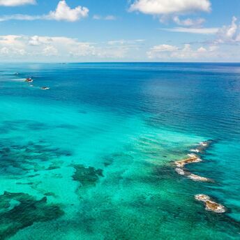 Aerial view of vibrant turquoise ocean waters with patches of coral reefs under a partly cloudy sky