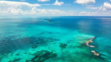 Aerial view of vibrant turquoise ocean waters with patches of coral reefs under a partly cloudy sky