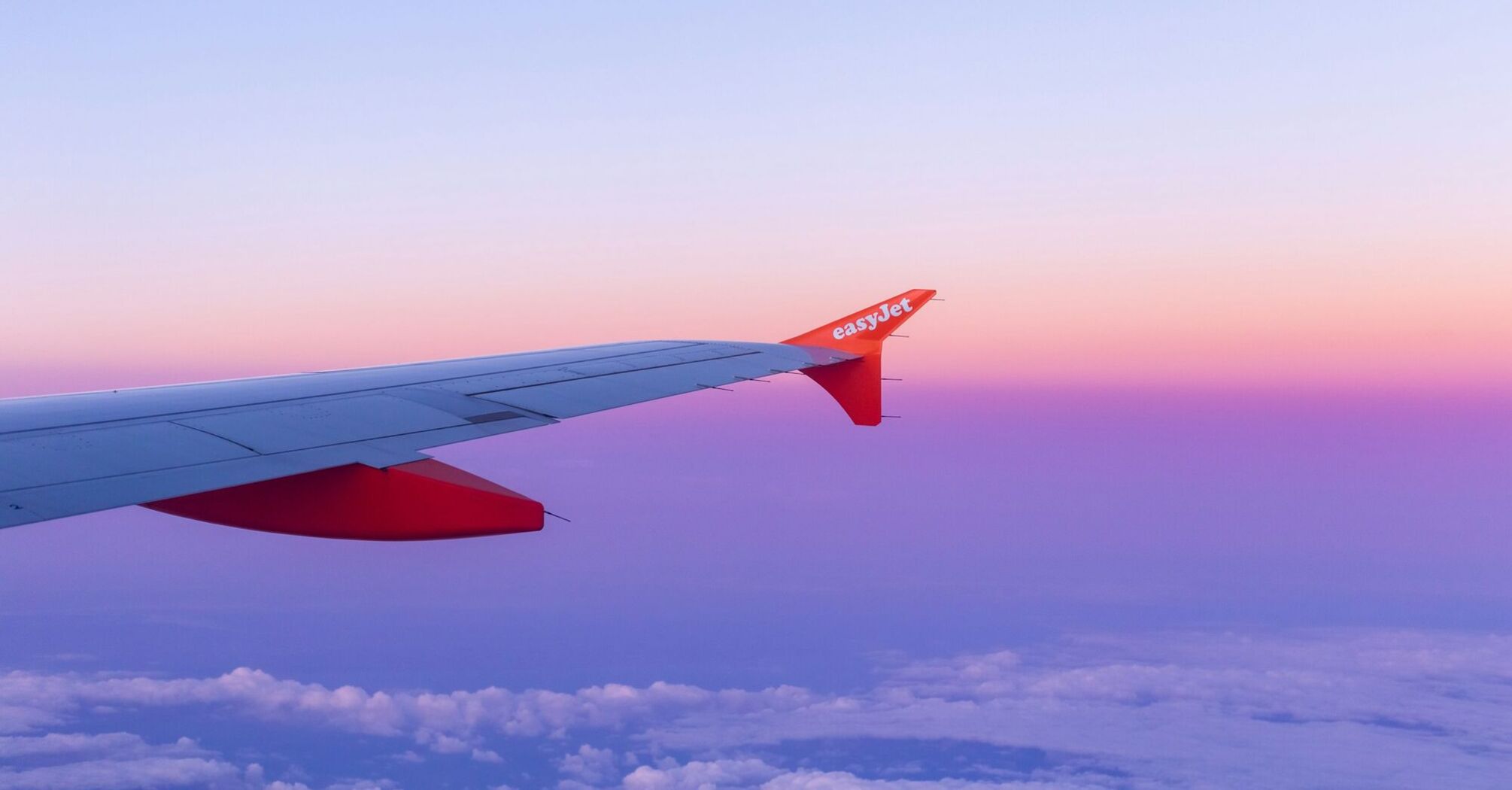 A view of an EasyJet airplane wing with a vibrant sunset sky in the background