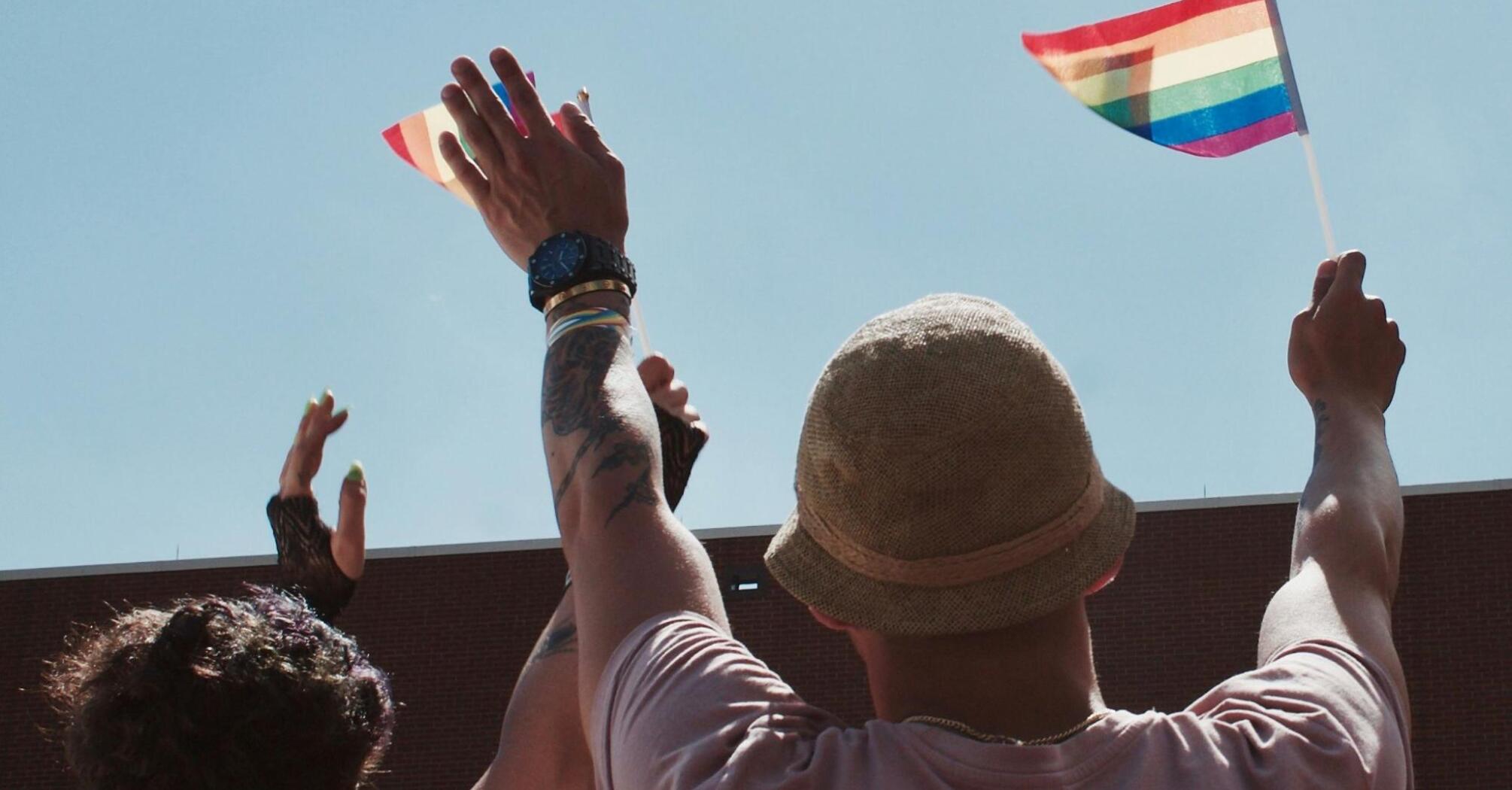 People raising rainbow flags at an outdoor LGBTQ+ event, celebrating inclusivity and pride under a clear blue sky