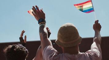 People raising rainbow flags at an outdoor LGBTQ+ event, celebrating inclusivity and pride under a clear blue sky