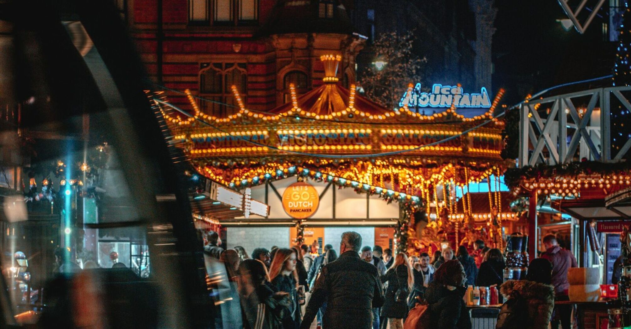 Visitors explore Nottingham's Winter Wonderland illuminated by festive lights, with a tram passing through Old Market Square