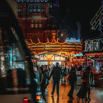 Visitors explore Nottingham's Winter Wonderland illuminated by festive lights, with a tram passing through Old Market Square