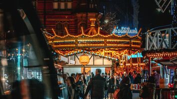 Visitors explore Nottingham's Winter Wonderland illuminated by festive lights, with a tram passing through Old Market Square