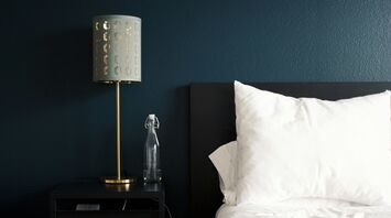 A cozy bedside table with a lamp, a clear water bottle, and a white pillow on a neatly made bed, evoking a calm and inviting atmosphere