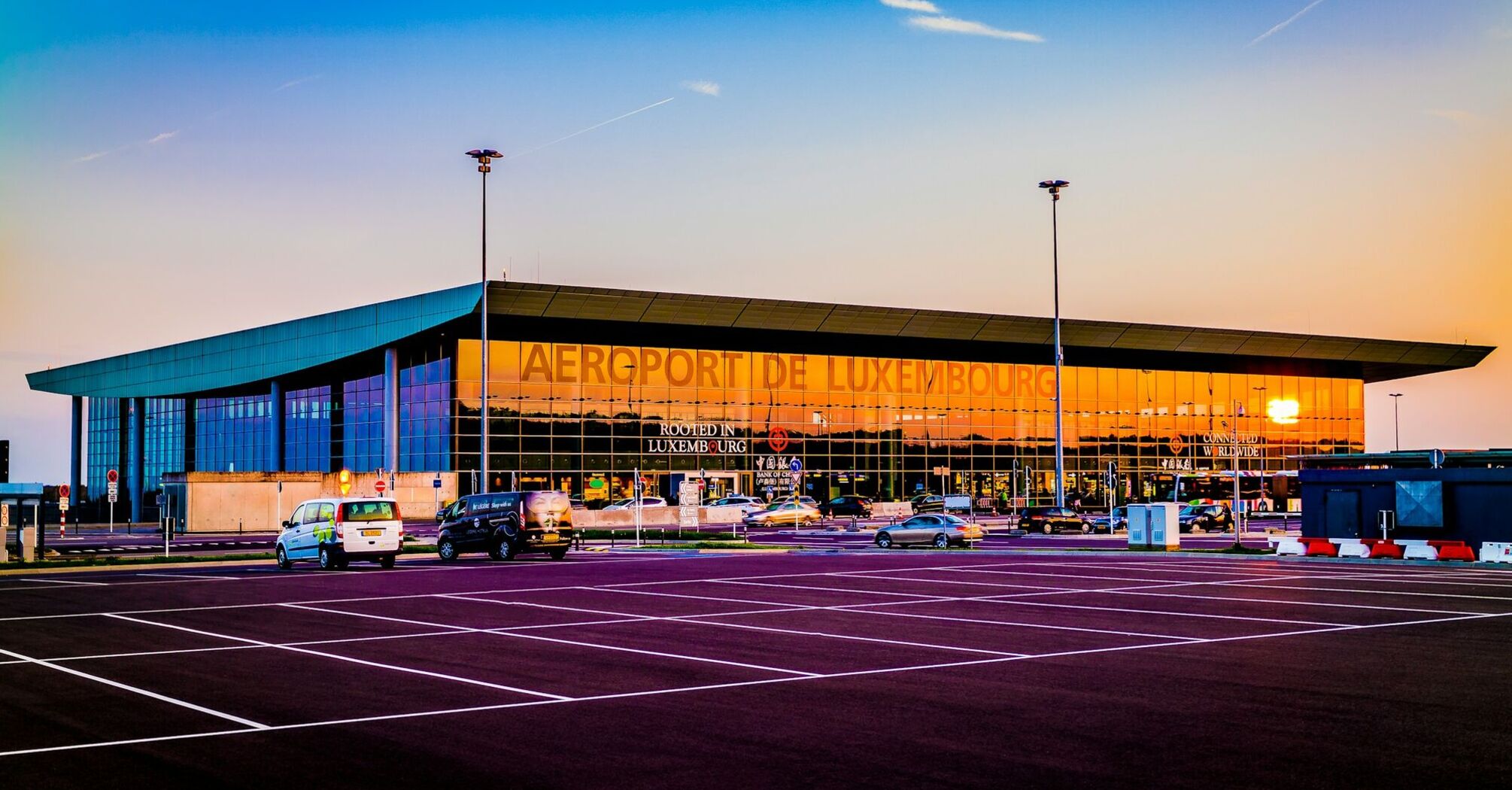 Luxembourg Airport exterior at sunset, showcasing modern architecture with parking space in the foreground